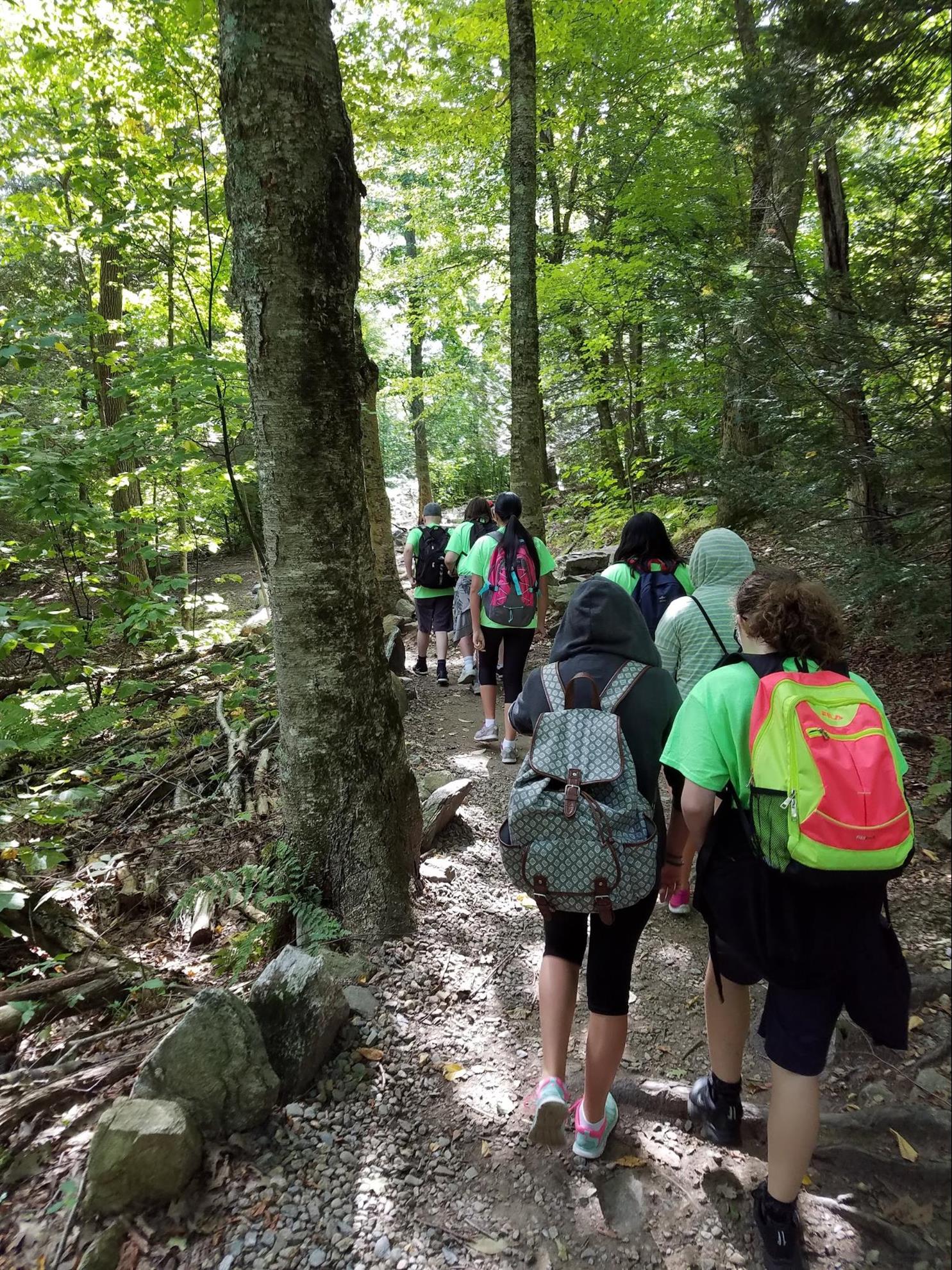 Line of students wearing matching shirts practicing computer science outdoors, walking along a trail